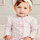 A baby wears the Kissy Kissy Baby Girls' Sea Shell Magic Zip Footie in soft Pima cotton with pastel seashell and starfish print, paired with a matching white headband, sitting indoors against a light background.