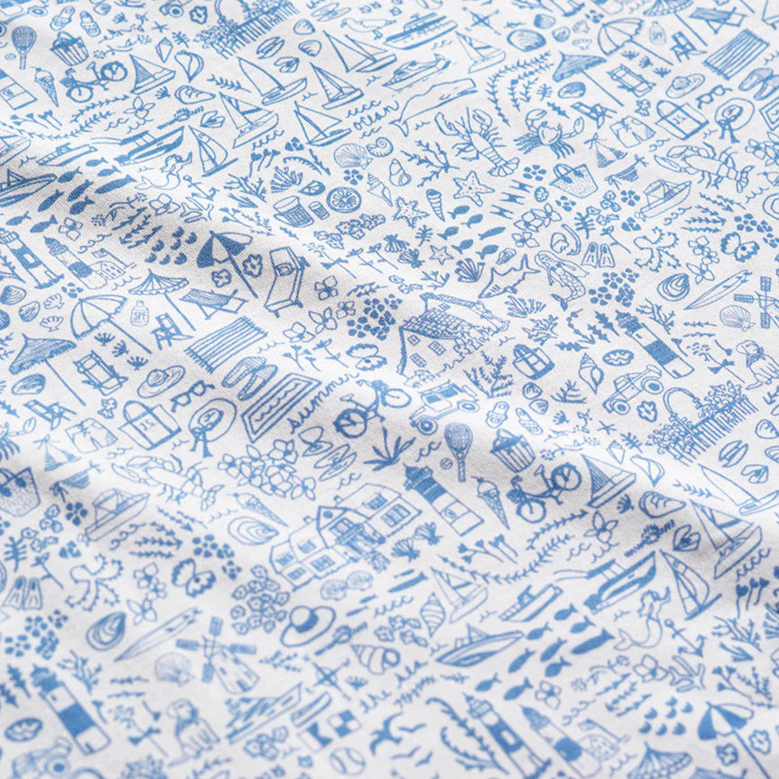 The Joy Street Baby Seaside Zip Onesie features white fabric with blue line illustrations of whimsical objects, houses, plants, animals, and outdoor scenes in a repeating Seaside print that captures summertime vibes.