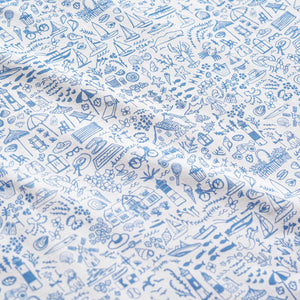 The Joy Street Baby Seaside Zip Onesie features white fabric with blue line illustrations of whimsical objects, houses, plants, animals, and outdoor scenes in a repeating Seaside print that captures summertime vibes.