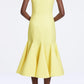 A person stands with hands behind their back, facing away from the camera, wearing the Seema Dress by Emilia Wickstead—a sleeveless, fitted yellow summer wool dress with a flared hem.