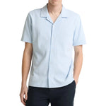 A man in a vince Seersucker Stripe Shortsleeve Cabana Shirt and dark pants stands against a white background.