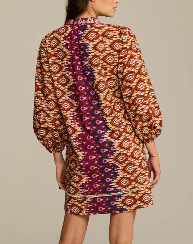 A woman is seen from the back wearing the Figue Hailey Dress—a relaxed fit, long-sleeve, knee-length style featuring geometric and ikat patterns in brown, orange, and purple.