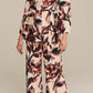 A woman in the Figue Avery Top, a long-sleeve printed viscose crepe wrap blouse, paired with matching wide-leg pants and heeled sandals, stands against a plain background.