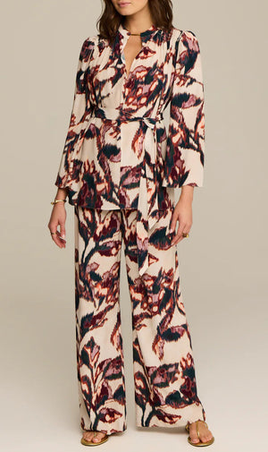 A woman in the Figue Avery Top, a long-sleeve printed viscose crepe wrap blouse, paired with matching wide-leg pants and heeled sandals, stands against a plain background.