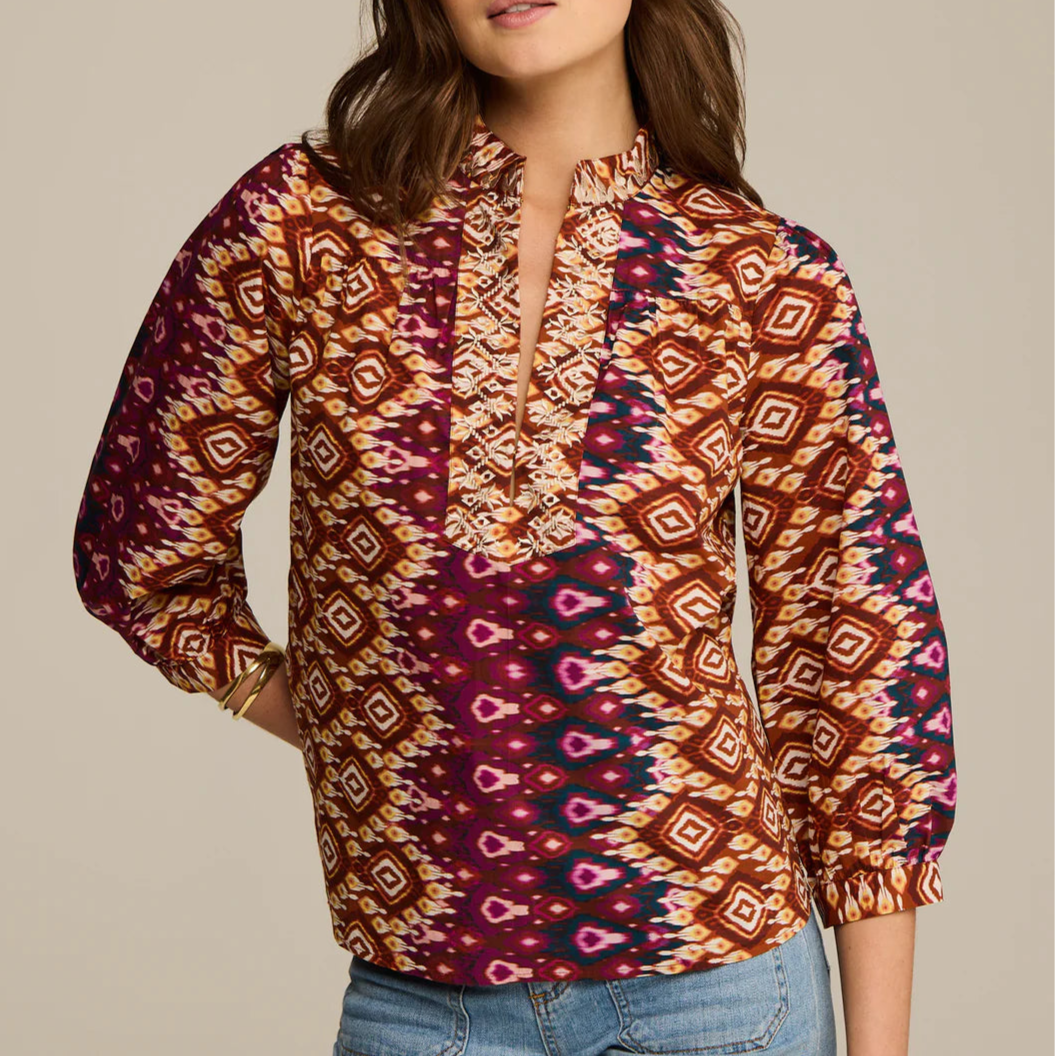 A woman wears the Figue Danilia Top, featuring a relaxed fit, notch collar, and ruffle trim, paired with light blue jeans.