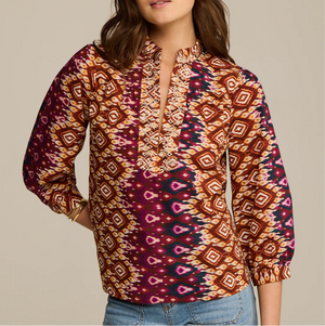 A woman wears the Figue Danilia Top, featuring a relaxed fit, notch collar, and ruffle trim, paired with light blue jeans.