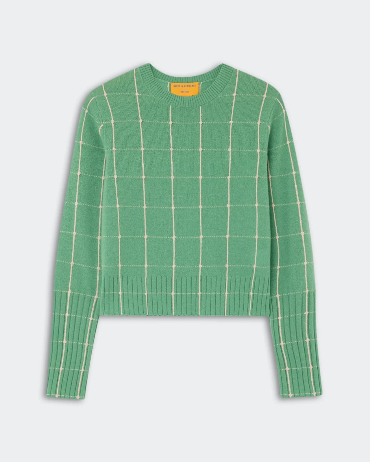 The Shrunken Checker Crew by Guest in Residence is a green women’s long-sleeve cashmere sweater with a white grid pattern, finished with ribbed cuffs and hem, shown against a plain white background.