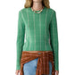 A person wearing the Shrunken Checker Crew cashmere sweater by Guest in Residence in green, paired with a beaded necklace, blue jeans, and a brown plaid shirt tied around the waist.