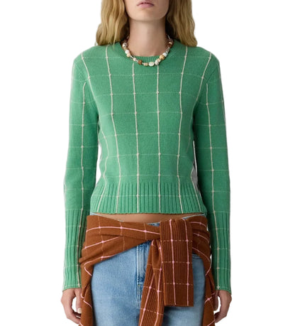 A person wearing the Shrunken Checker Crew cashmere sweater by Guest in Residence in green, paired with a beaded necklace, blue jeans, and a brown plaid shirt tied around the waist.