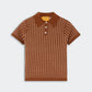 The Shrunken Waffle Polo by Guest in Residence is a brown, short-sleeve cashmere knit shirt featuring a white dotted pattern, button-up collar, ribbed edges, and a subtle waffle texture, shown against a plain light background.