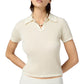 A woman wears the Guest in Residence Shrunken Cashmere Polo in off-white, featuring a lightweight waffle knit, short sleeves, and a collar. She pairs it with a beaded necklace and stands with her arms behind her back.