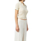 A woman wears the Guest in Residence Shrunken Cashmere Polo in cream with high-waisted cream pants, standing against a white background.
