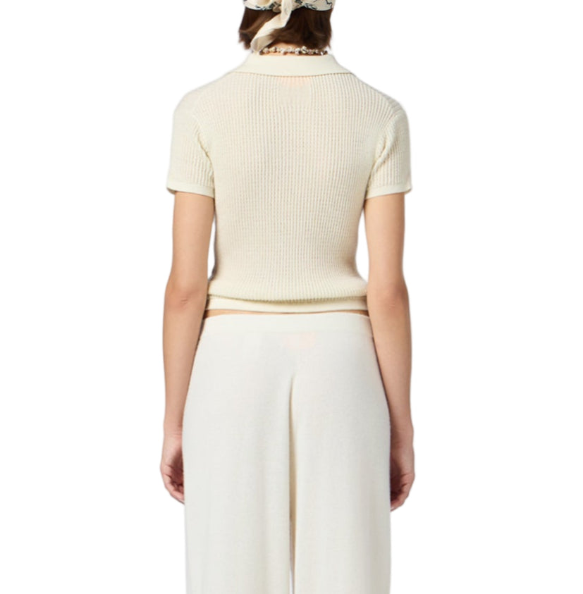 A person faces away from the camera, dressed in the Guest in Residence Shrunken Cashmere Polo, wide-leg cream pants, and a light-colored headscarf, set against a white background.