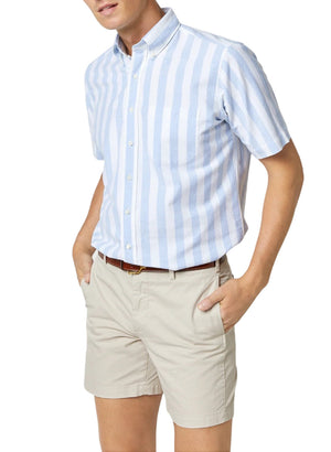 A person wearing a light blue and white Sid Mashburn Short-Sleeved Button-Down Sport Shirt with a nonfused button-down collar, paired with beige shorts, hands in pockets, exuding that classic beach boys vibe.