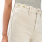 A person wears the Rag & Bone Skylar High Rise Trouser Jean in light beige, crafted from vintage stretch denim with a gold buckle detail near the waistband, paired with a striped sleeveless top.