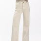 A person wears Rag & Bone's Skylar High Rise Trouser Jean in beige vintage stretch denim, paired with a short-sleeve striped shirt and black pointed shoes, standing against a plain white background.