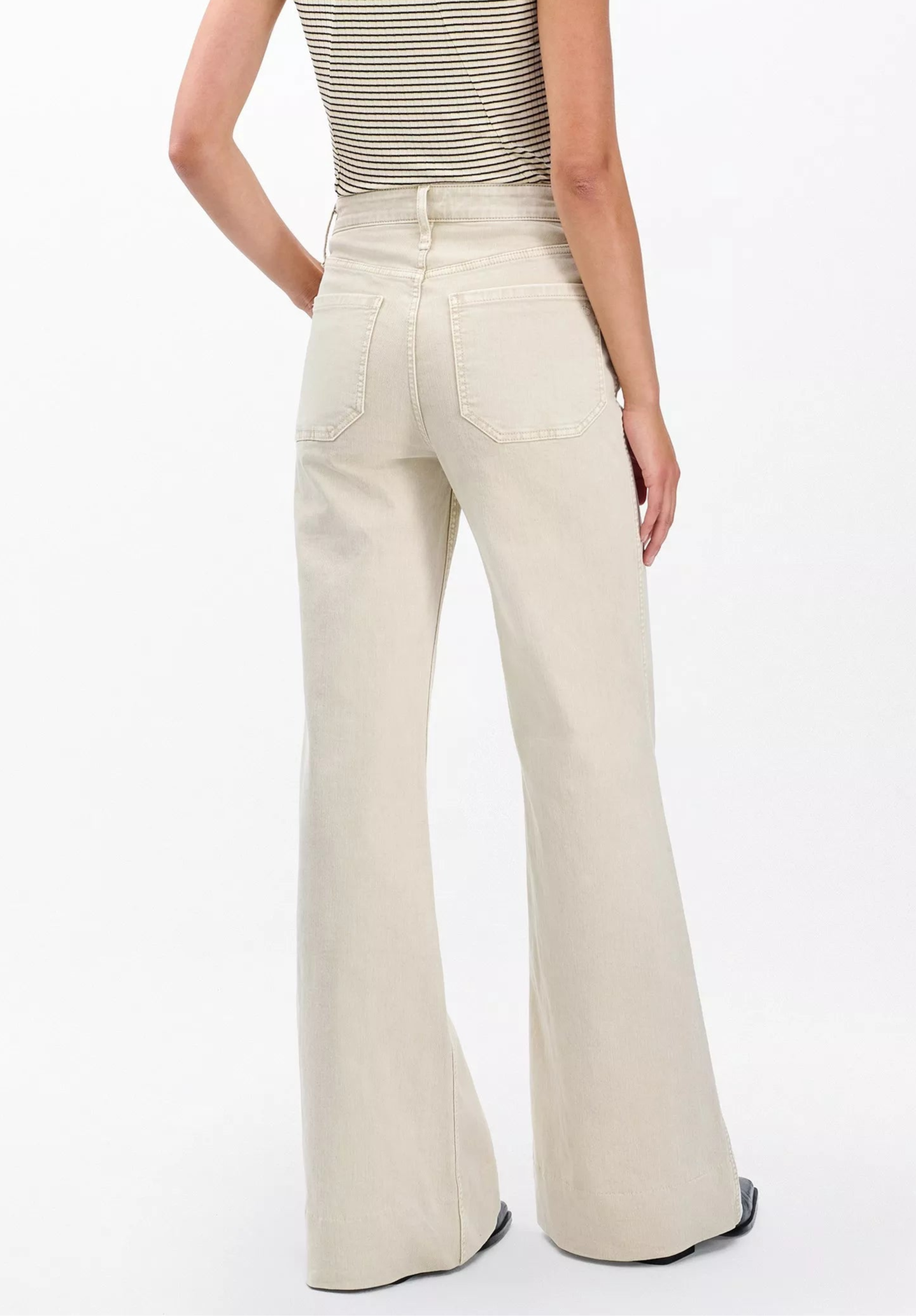 A person stands facing away, wearing Rag & Bone's Skylar High Rise Trouser Jean in vintage stretch denim with a sleeveless striped top, showcasing the back view of the outfit.