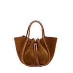 The Proenza Schouler Small Ruched Soft Suede Tote, crafted in brown suede with leather handles and a drawstring closure, showcases a sculptural silhouette reminiscent of a small ruched tote and is displayed against a white background.
