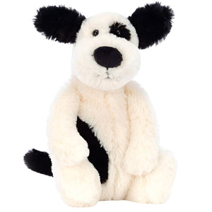 The Jellycat Bashful Black & White Puppy, Small, is an adorable plush toy dog featuring soft white fur, black floppy ears, a spot around one eye, and a black patch on its side, sitting upright.