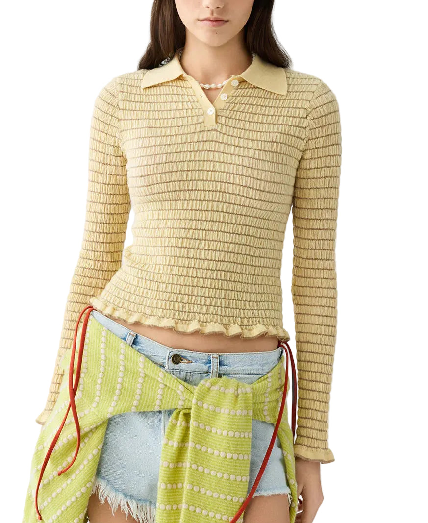 A woman wearing the Guest in Residence Smocked Long Sleeve Shrunken Polo in beige, paired with a distressed denim skirt and a green sweater tied at the waist.