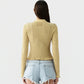 A person with long brown hair, wearing the Guest in Residence Smocked Long Sleeve Shrunken Polo in yellow and light blue frayed denim shorts, stands with their back to the camera against a plain light background.