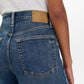 A person shown from the back wears Rag & Bone's Sofie High Rise Full Length Cuff jeans in blue denim and a white shirt. The wide leg jeans feature a large back pocket with subtle stitching and a tan leather patch on the waistband.