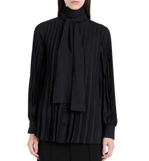 A person wears the Soomin Technical Crepe Top by Proenza Schouler, a long-sleeved black blouse with accordion pleats and a matching neck scarf, shown from the waist up.