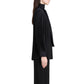 A person stands in profile against a white background wearing the Proenza Schouler Soomin Technical Crepe Top in black, paired with black pants.