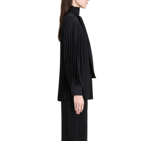 A person stands in profile against a white background wearing the Proenza Schouler Soomin Technical Crepe Top in black, paired with black pants.