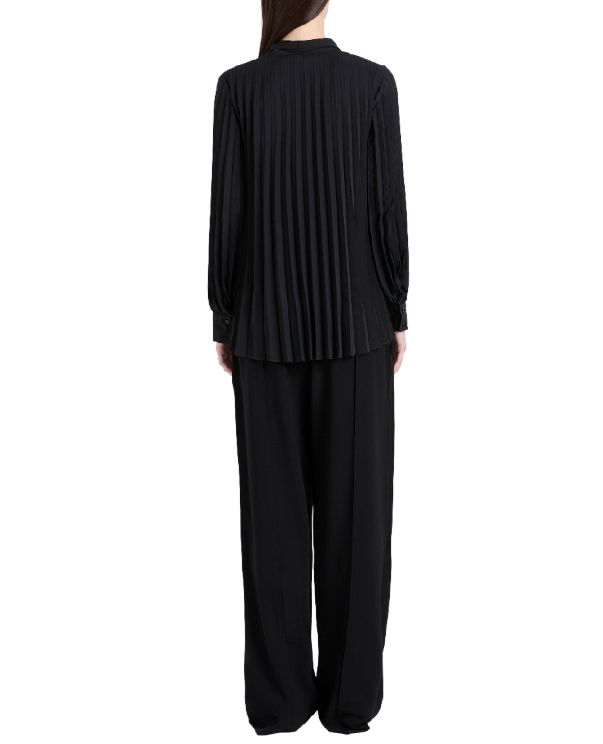 A person stands with their back to the camera in a black Proenza Schouler Soomin Technical Crepe Top and loose black pants, set against a white background.