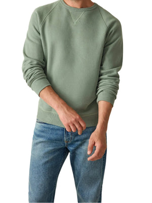 A person wearing the Faherty High Standard Fleece Crewneck in green, made from organic pima cotton, paired with blue jeans stands against a plain background.