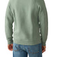 A person is pictured from the back in a sage green Faherty High Standard Fleece Crewneck sweatshirt, made from organic cotton, and blue jeans.