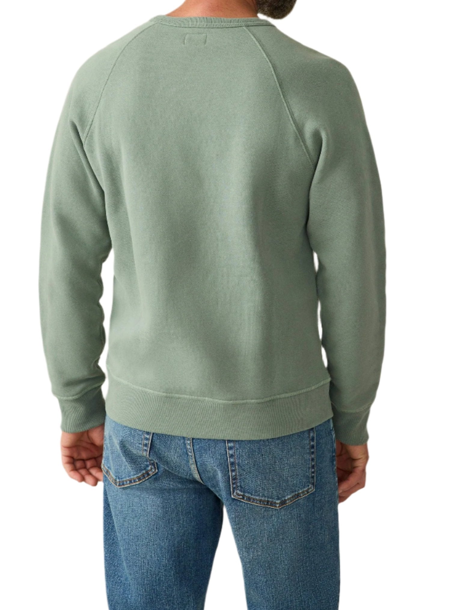 A person is pictured from the back in a sage green Faherty High Standard Fleece Crewneck sweatshirt, made from organic cotton, and blue jeans.