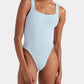 Model wears the Hunza G Square Neck Swim, a light blue crinkle fabric one-piece with high-cut legs and wide straps, posed against a plain white background.