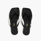 The Lily Square Toe Croc Sandal by Tkees features a square toe, thin straps, and black crocodile-embossed leather. The insole is adorned with the Tkees brand name in gold lettering for an elegant touch.