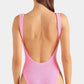 A person with long brown hair is seen from behind, wearing the Hunza G Square Neck Swim, a pink, textured one-piece swimsuit crafted from the brand’s Original Crinkle fabric, against a plain background.