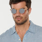 A man wearing Krewe St. Louis Mirrored Sunglasses—iconic classic round gold frames with mirrored lenses—and a light blue button-up shirt looks straight ahead against a plain background.