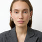 A woman with straight brown hair wearing a grey blazer and Lie Studio Steffie Earrings in sterling silver looks directly at the camera against a plain white background.