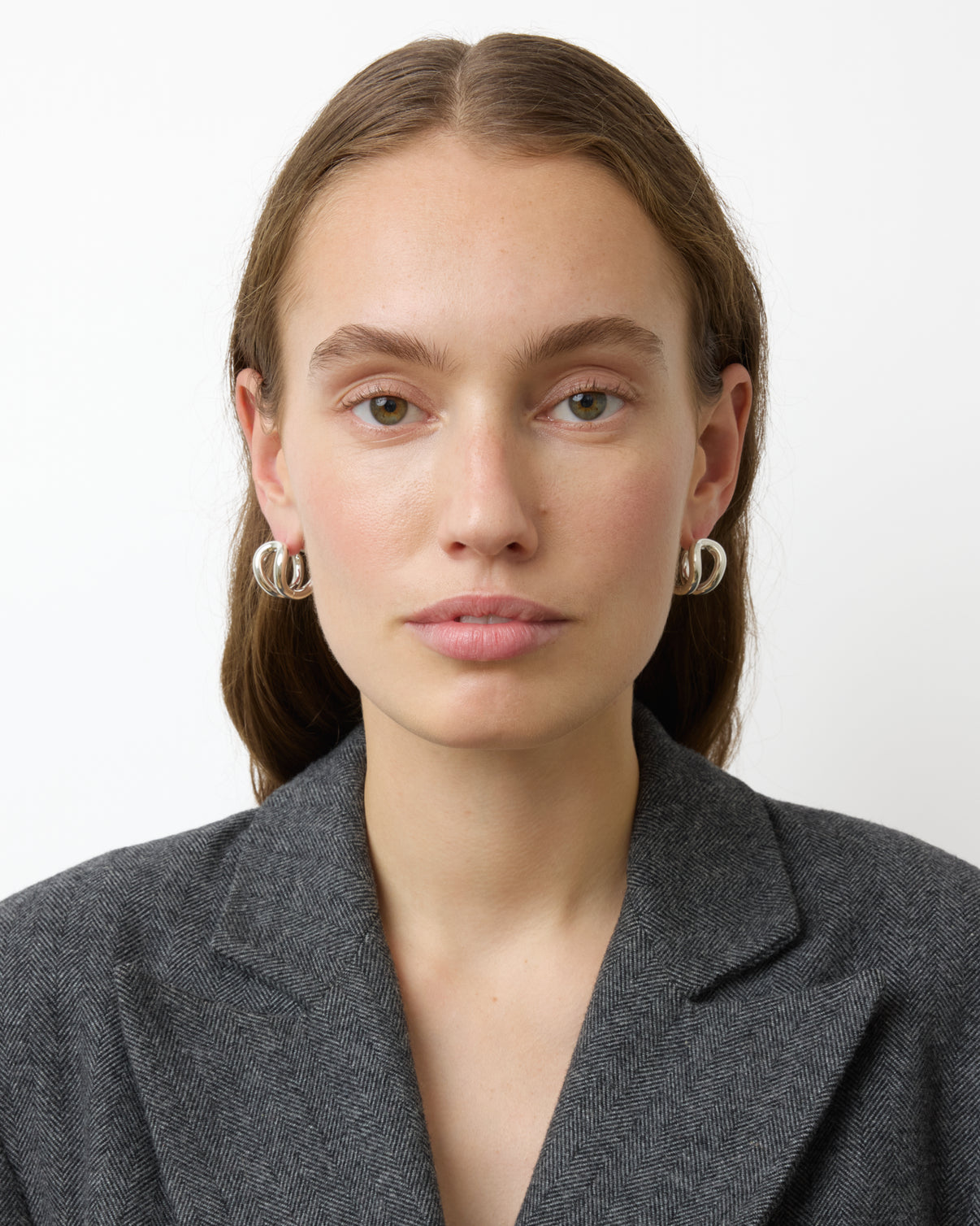 A woman with straight brown hair wearing a grey blazer and Lie Studio Steffie Earrings in sterling silver looks directly at the camera against a plain white background.