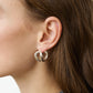 Close-up of a person with brown hair wearing Lie Studio's Steffie Earrings—large, sterling silver double hoops—in their left ear. The individual is dressed in a grey textured garment.