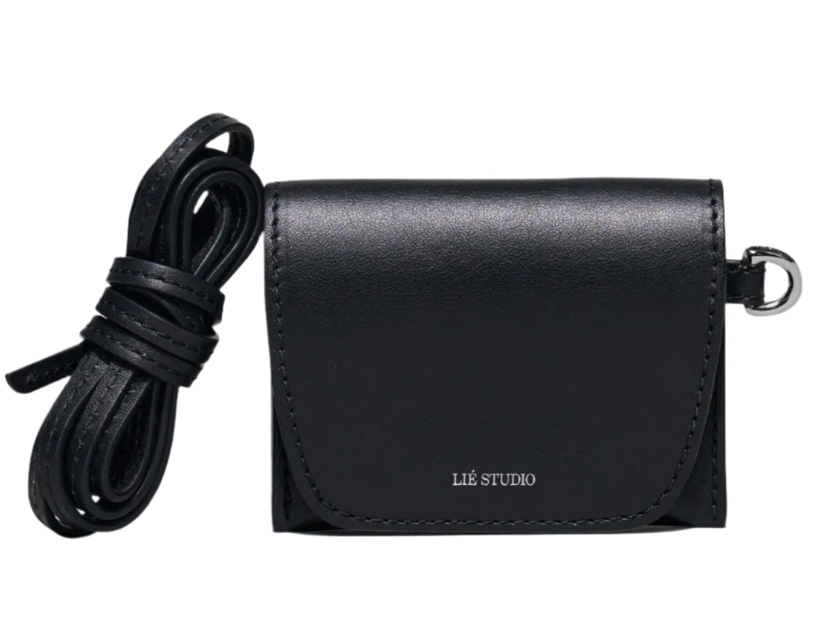 The Lie Studio Stella Wallet is a compact black crossbody bag made from Italian cow leather with a flap closure, detachable strap, and "LIÉ STUDIO" logo embossed on the front—a sophisticated and versatile accessory.