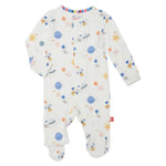 Introducing the Magnetic Me Stellar Tails Footie, a white baby onesie designed with an enchanting space-themed pattern, showcasing planets, rockets, and stars in hues of blue, orange, and yellow. Crafted from eco-friendly TENCEL™ modal and featuring SewSafe™ magnetic closures for effortless dressing.