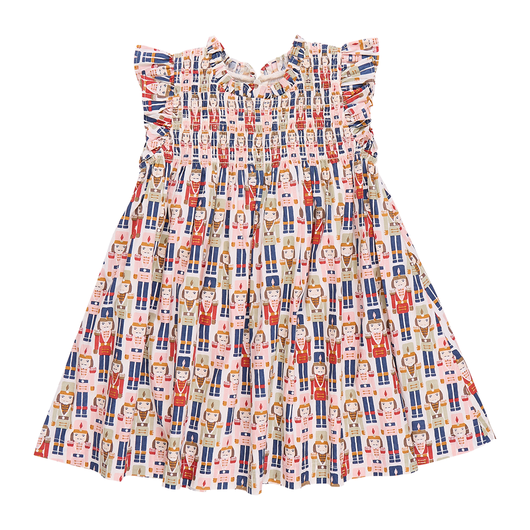 The Pink Chicken Girls Stevie Dress by Pink Chicken showcases a vibrant pattern of illustrated figures dressed in various outfits, evoking the charm of a Vintage Nutcracker. It is accented with ruffled sleeves, a gathered neckline, and intricate smocked detailing for an added touch of elegance.