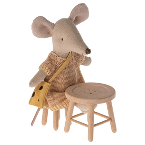 A fabric mouse doll in a knitted dress with a yellow bag sits on a wooden chair from the Mouse Hole Farmhouse collection next to the Maileg Table and Stool Set, Mouse.