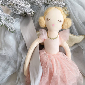 The MON AMI Sugar Plum Fairy by Mon Ami lies gracefully next to frosted evergreen branches, adorned with a gold crown, blonde hair, and a pink tulle dress that captures the enchantment of a ballet dancer against light blue fabric.