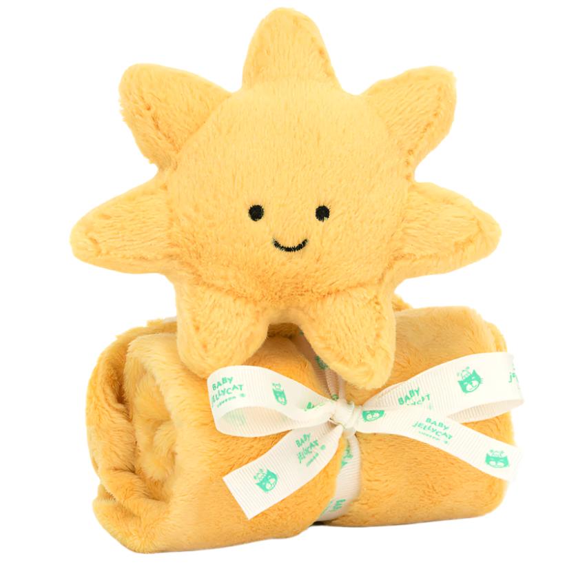 The Jellycat Amuseables Sun Soother, a soft and plush sun with a smiling face, sits on a rolled yellow blanket made from recycled fibers and tied with a ribbon that reads "Baby Blanket." Perfect as a newborn gift.