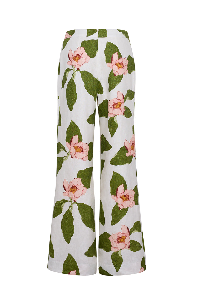 The Cara Cara Sunflower Pant features a green and pink floral print with large leaves and flowers. These white wide-leg pants offer a tailored, fresh, and vibrant look, displayed against a plain background.