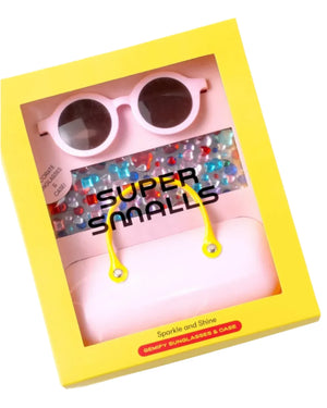 The yellow box showcases the Super Smalls Sparkle and Shine Gemify Sunglasses in pink, complete with UVA/UVB protection. Nestled alongside the sunglasses is a stylish pink case and vibrant beads. Decorated with gem stickers, it epitomizes the ultimate sparkle and shine under the "Super Smalls" brand label.