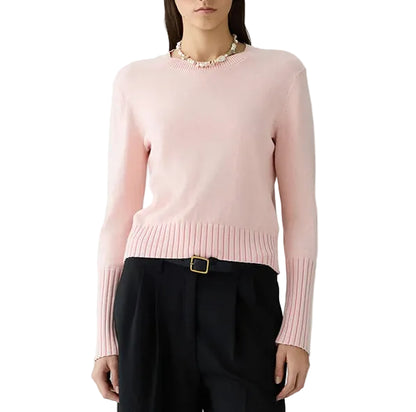 A person wearing the Sunwash Shrunken Crew sweater in light pink by Guest in Residence, paired with black belted pants, stands against a white background.