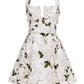 The Agua Dress by Agua By Aguabendita is a sleeveless floral piece featuring a fitted bodice, flared skirt, and sweetheart neckline, with pink flowers and green leaves on a white background.